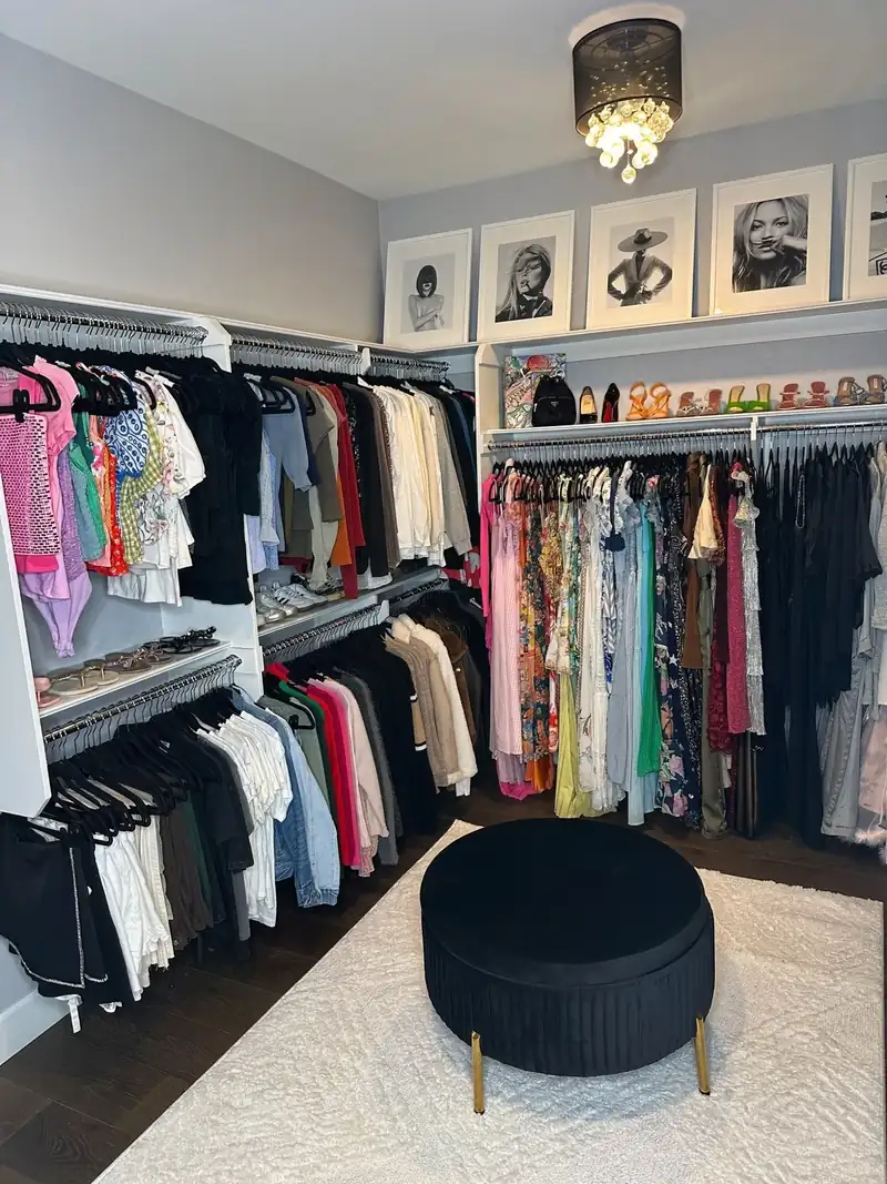 After: Huntington Beach walk-in closet with clothes hung by color under framed black and white prints and a round velvet ottoman