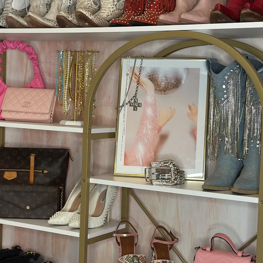 Gold shelving with cowboy boots and designer bags in a walk-in closet