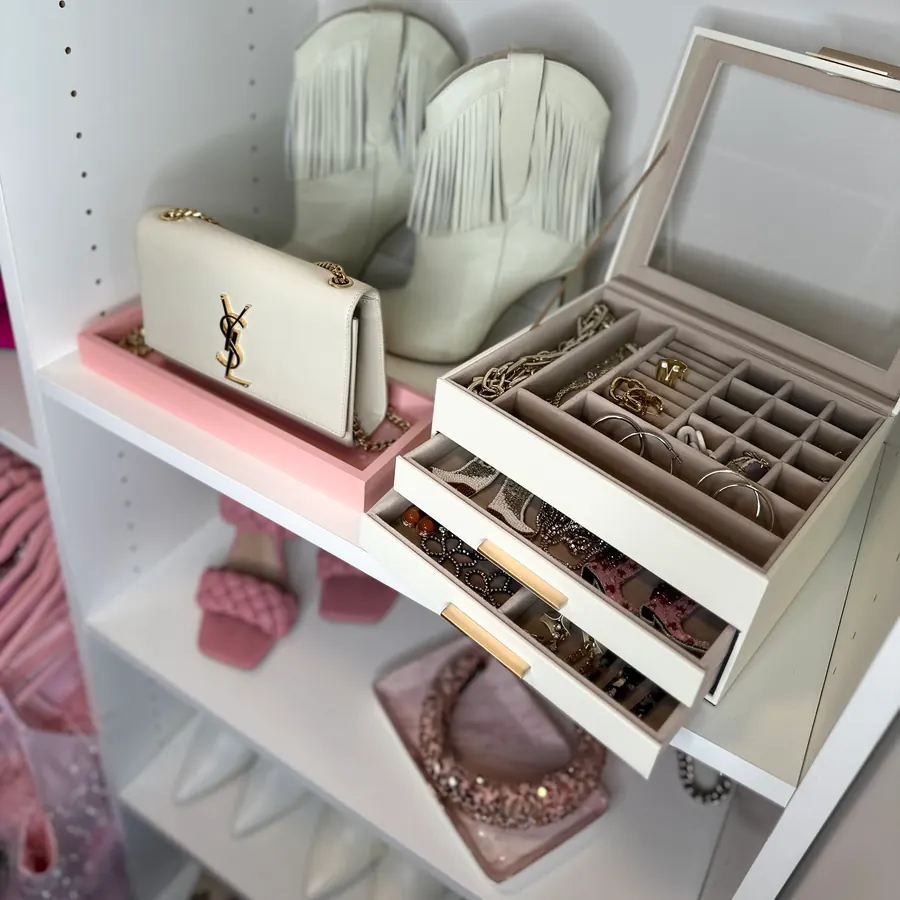 Saint Laurent bag on a pink tray beside white fringe boots and an open jewelry box